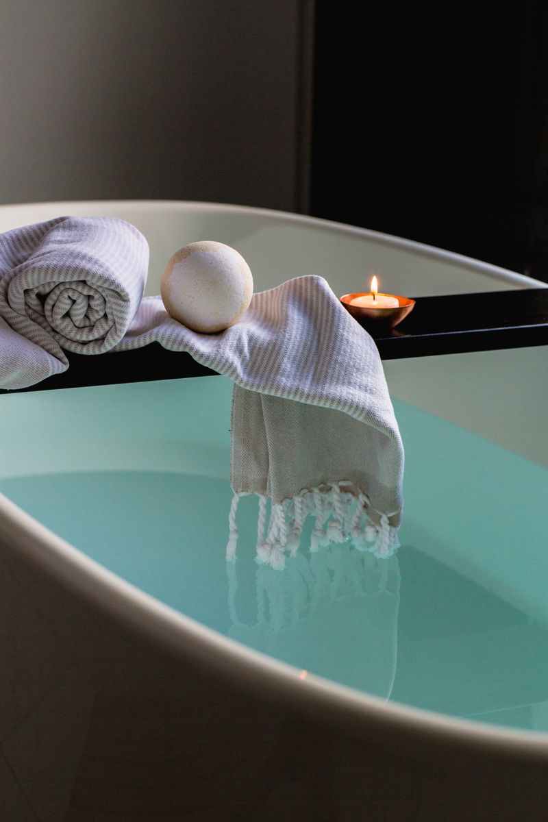 A folded towel and lit candle on the edge of a bath